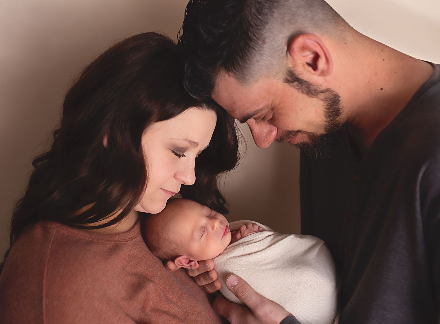 Parents gazing lovingly at their newborn baby in a warm, intimate portrait session .newborn photography near me