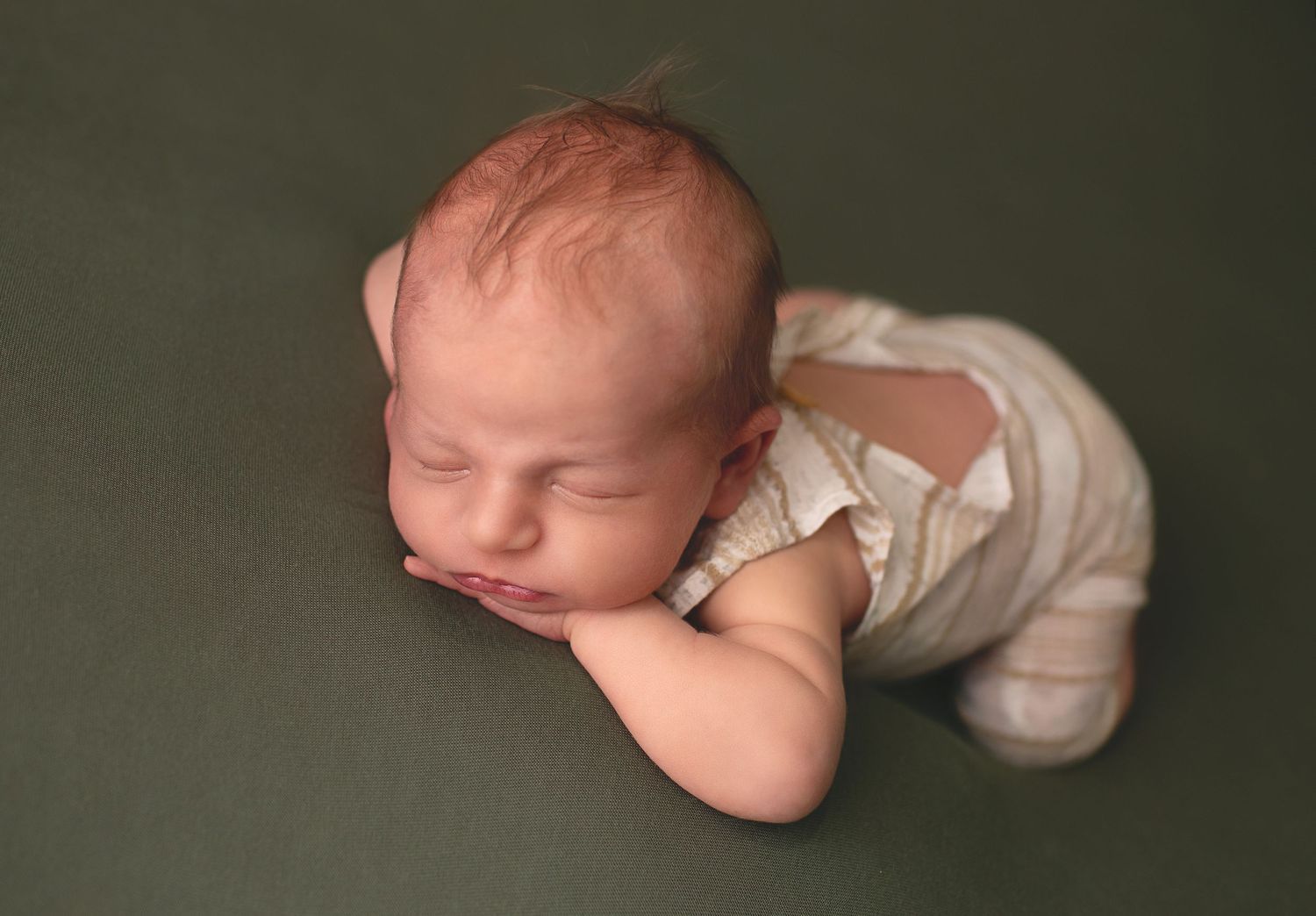 Sleeping newborn baby in light-colored outfit lying peacefully on dark gray backdrop during professional photo session.