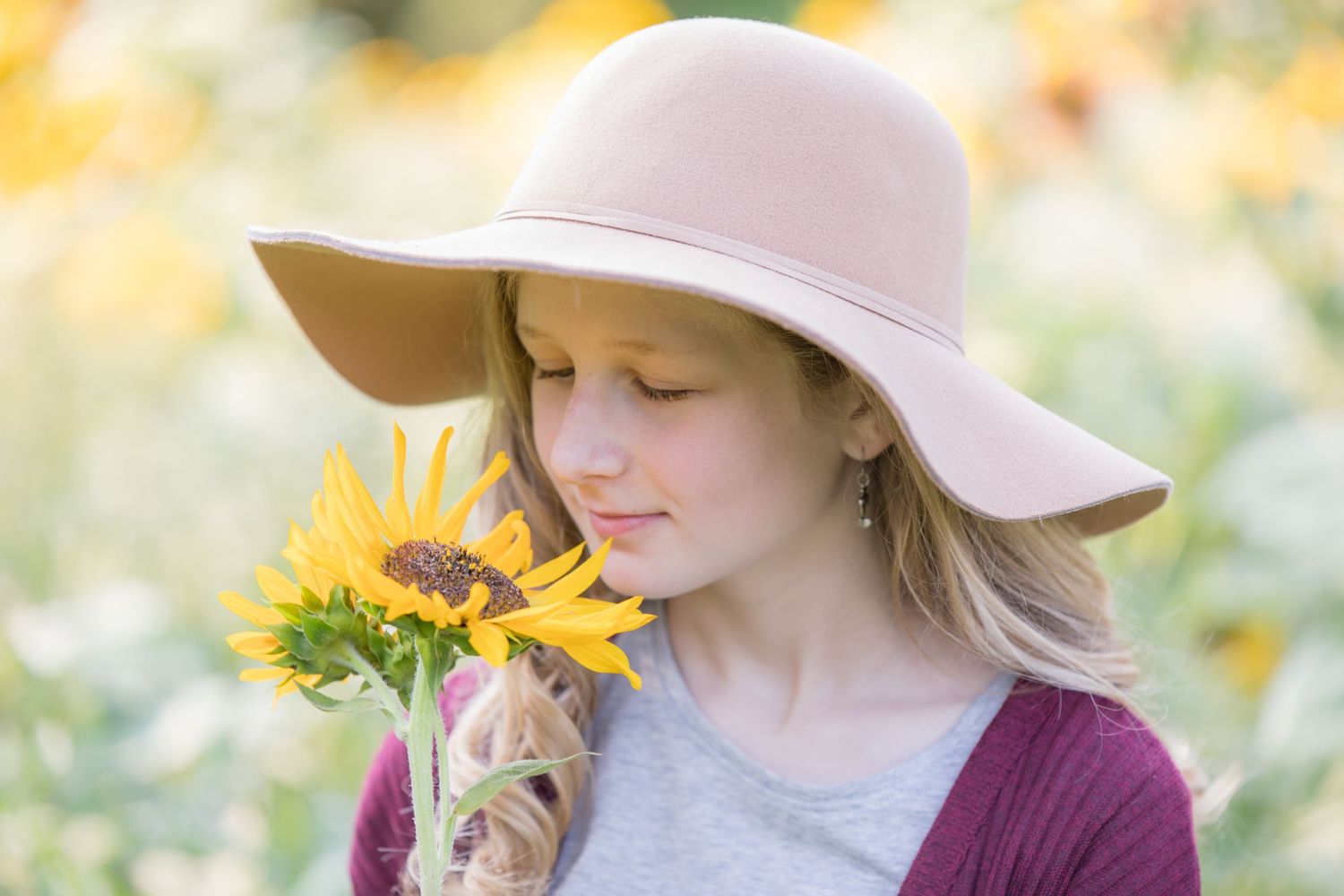 girl in hat smelling sunflower in field at ward's farm in salem new jersey in bright sun light