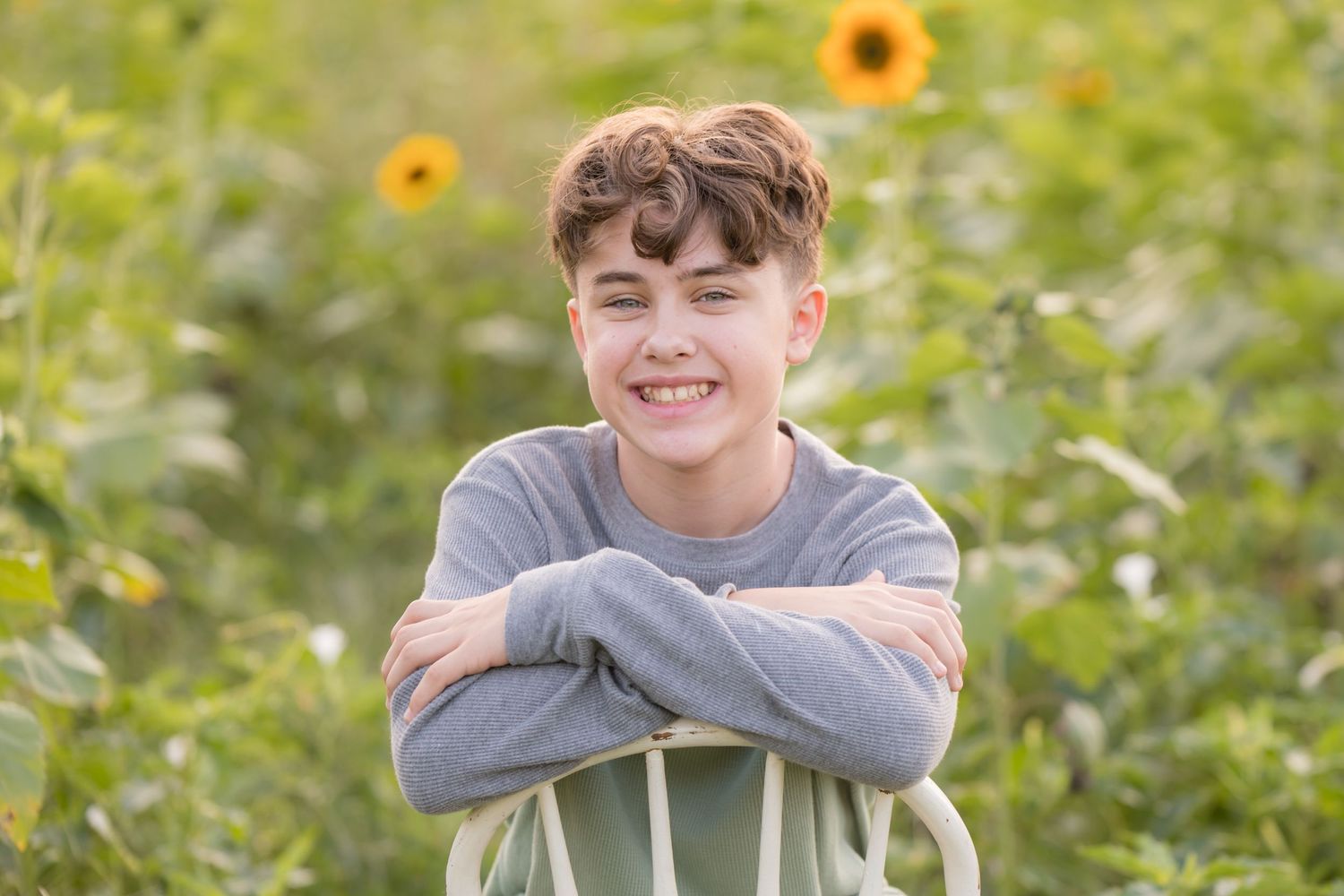 teenage boy sitting backwards on chair in sunflower field at Ward's Farm in Salem New Jersey at sunset