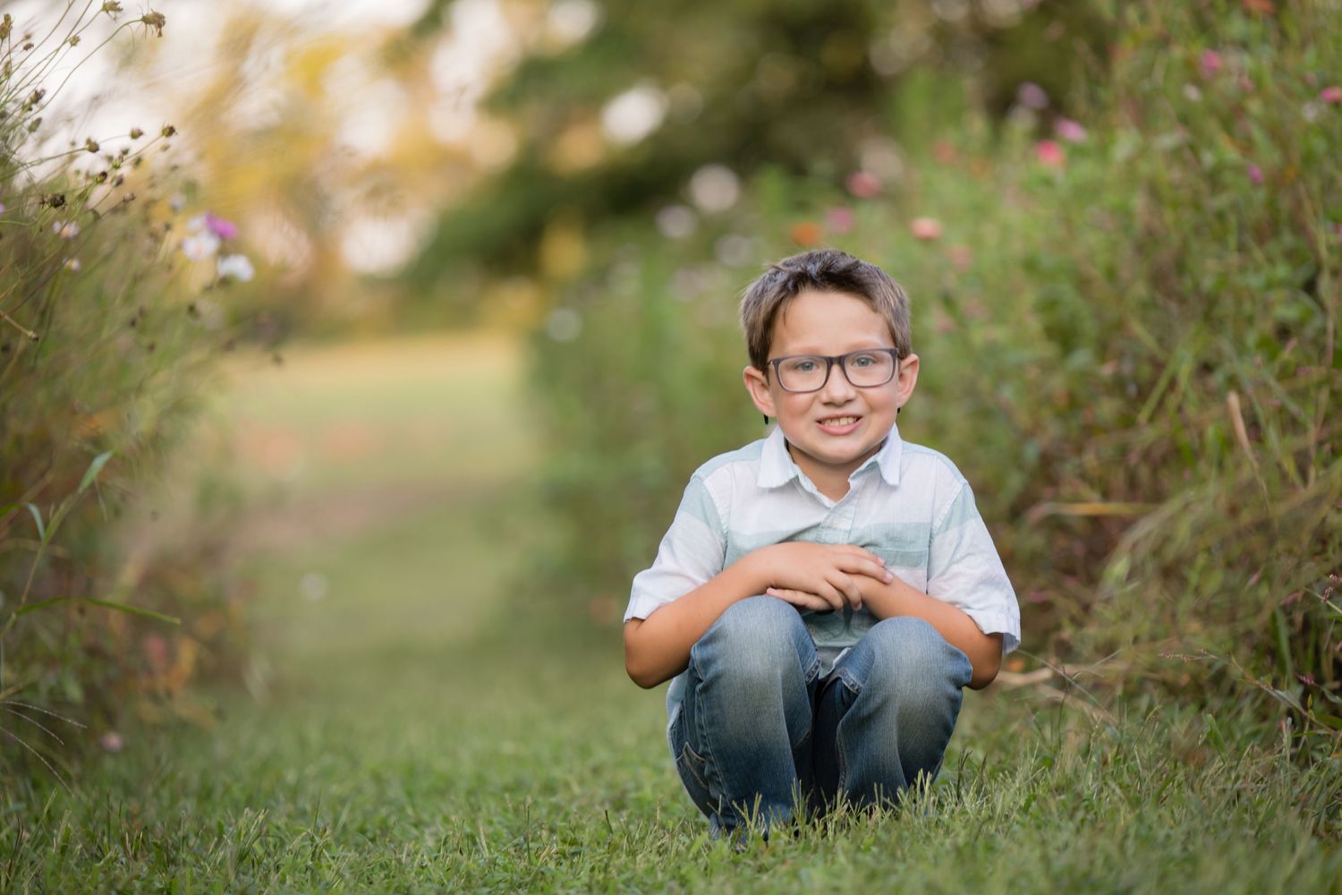 young boy in glasses squatting in wildflower zinnia field at ward's farm in salem new jersey at sunset