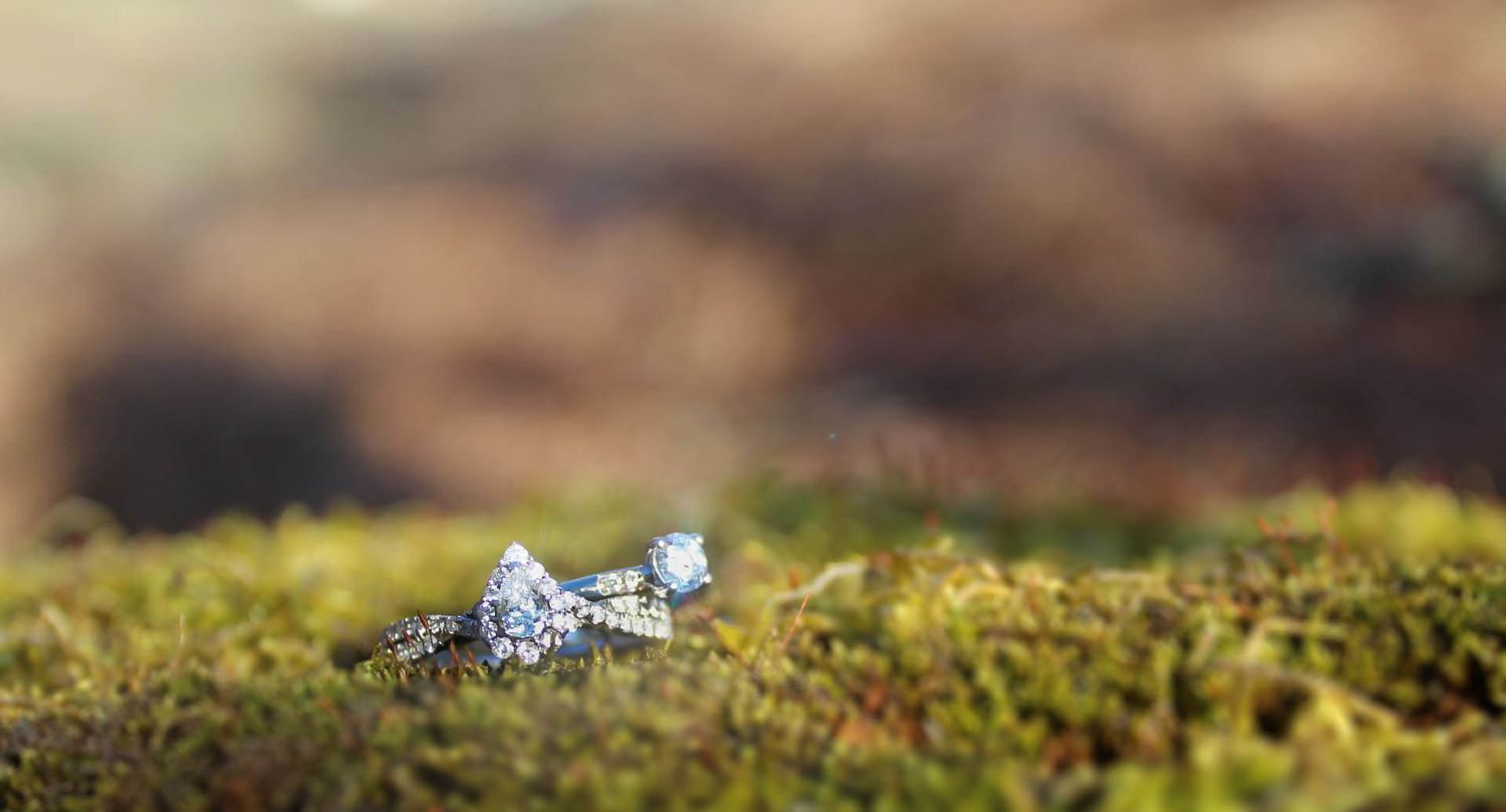Diamond engagement ring photographed in soft focus on green moss with natural bokeh.
