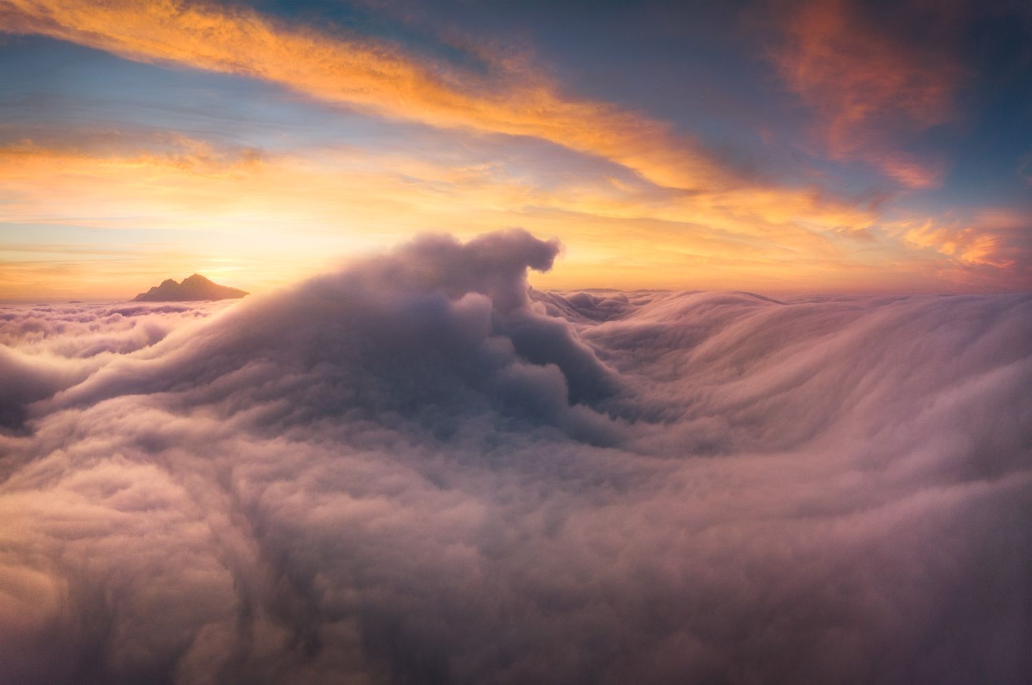 Dramatic sunset illuminates billowing clouds from above creating a dreamlike ocean of orange sky.