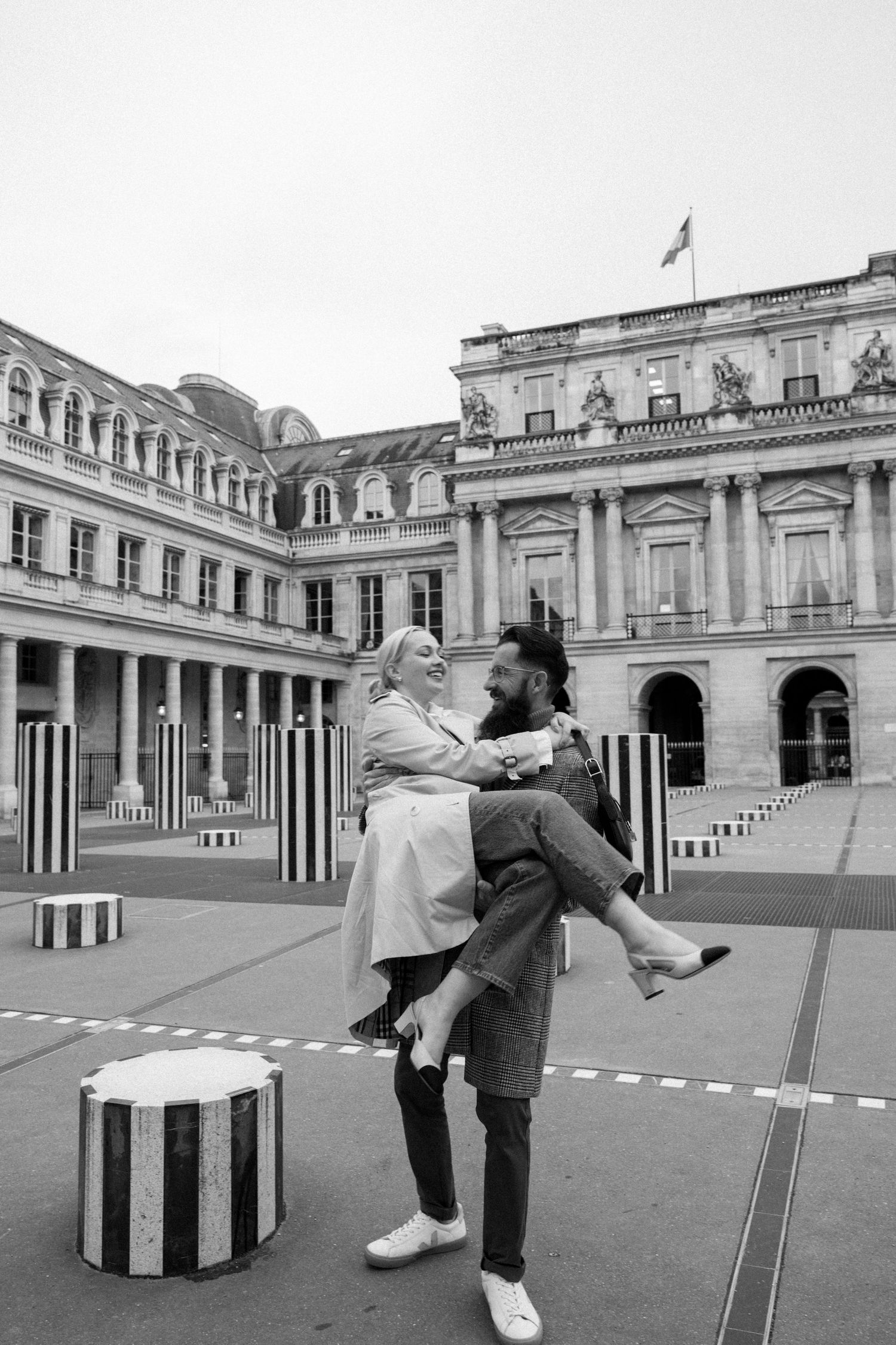 Playful couple enjoys a moment at the Palais Royal's striped columns in Paris.