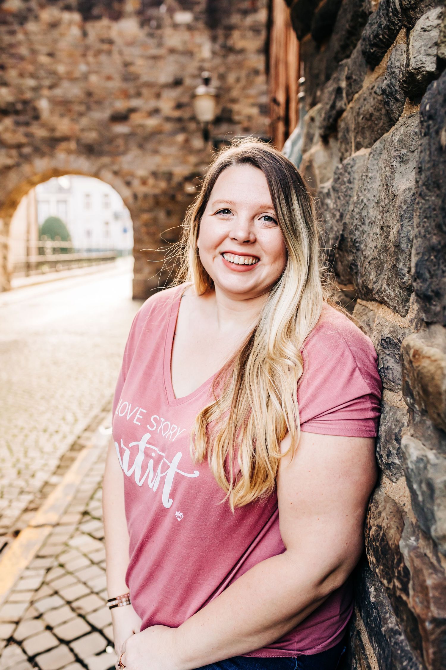 Portrait of person smiling against stone wall with archway in background.