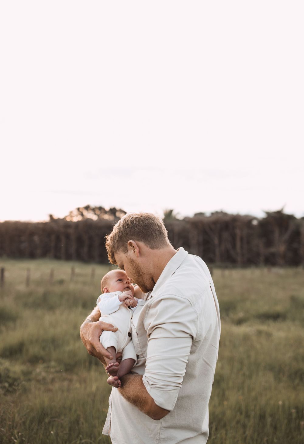 A tender family moment captured in a grassy field at sunset showing affection with a newborn baby.