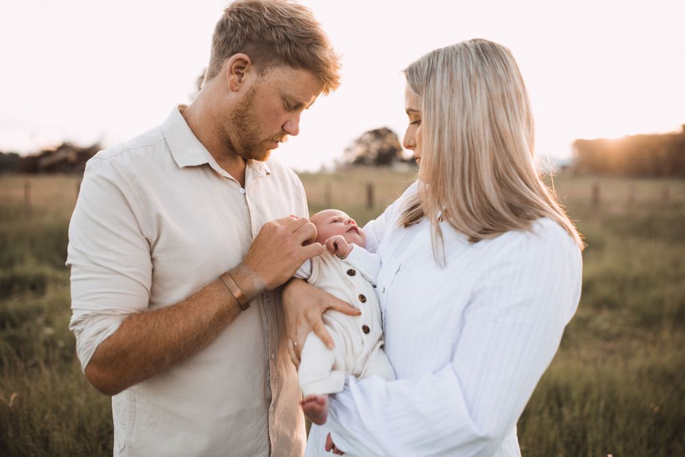 Parents sharing a tender moment with their newborn baby in a sunlit field.