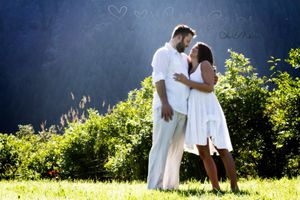 Couple in white clothing sharing intimate moment against blue sky background.