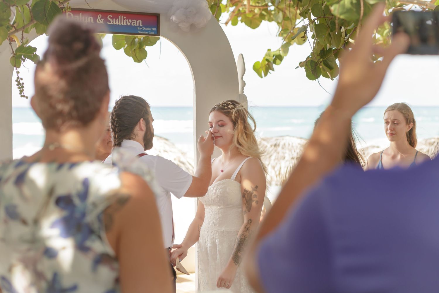 Destination wedding photo in Cuba with groom wiping tears from bride's face. Beach behind them.