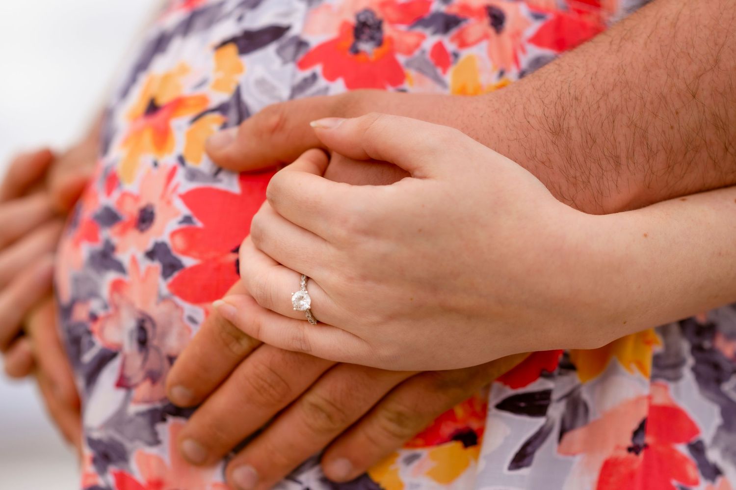 Close-up of hands with engagement ring against floral print dress.