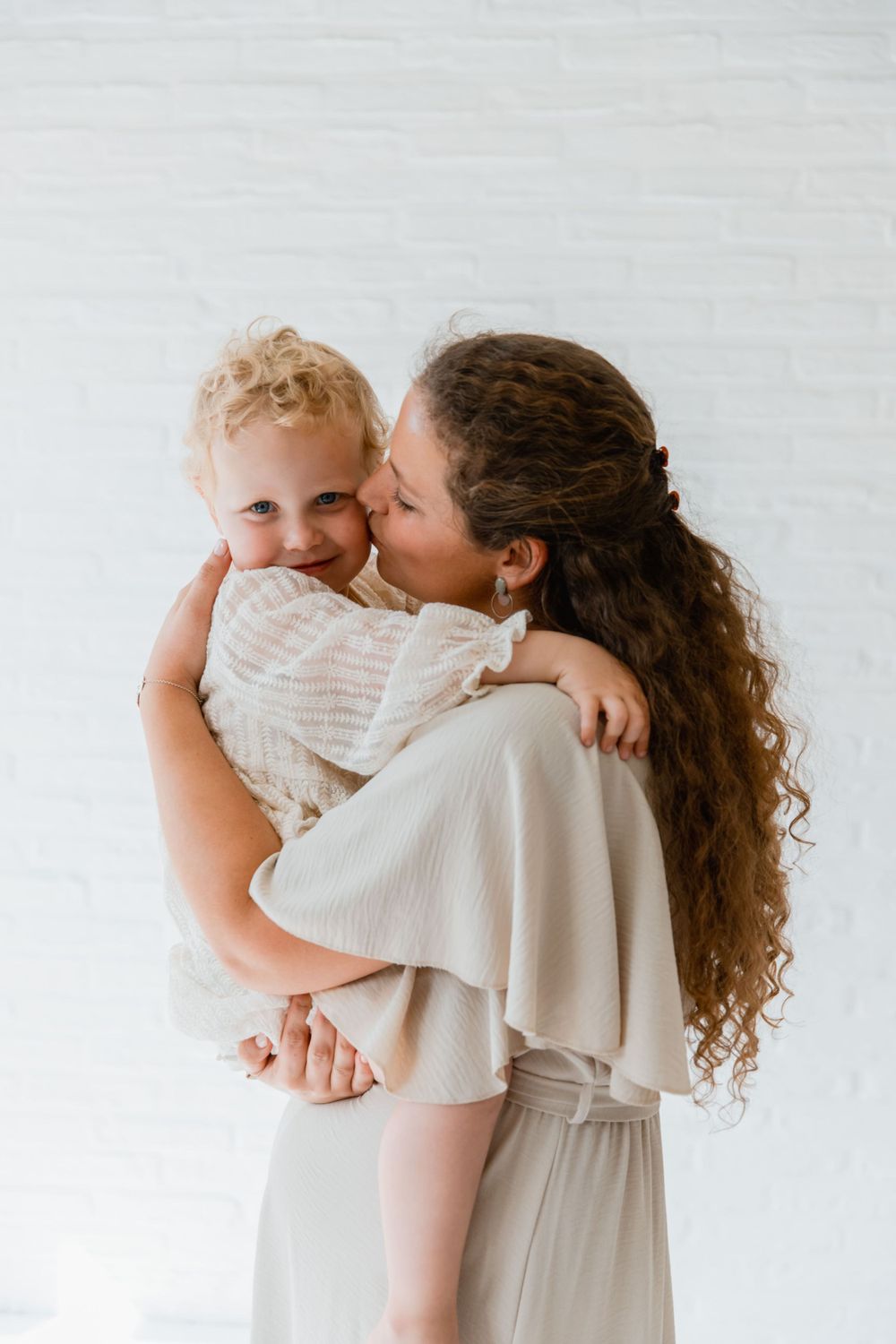 Tender moment between parent and child in white outfits against light background.