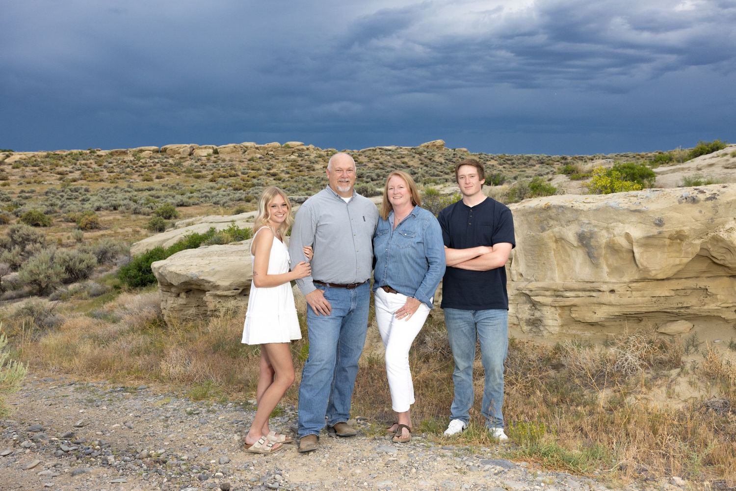 Small group posed together in desert landscape with dramatic cloudy sky and rocky terrain.