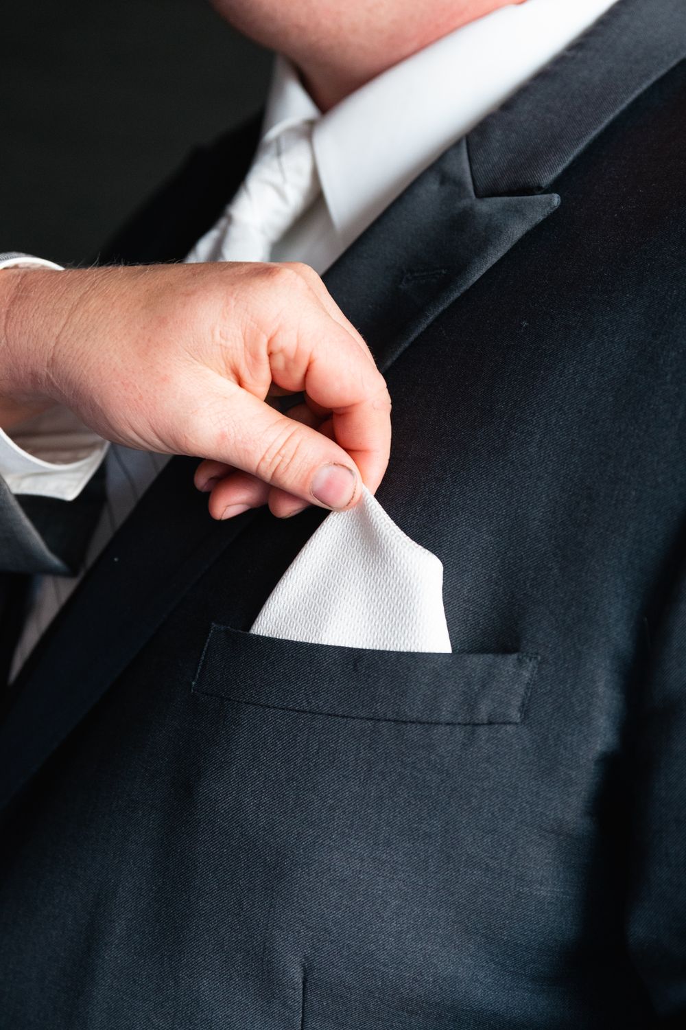 Close-up of a white pocket square being adjusted in a black suit jacket.