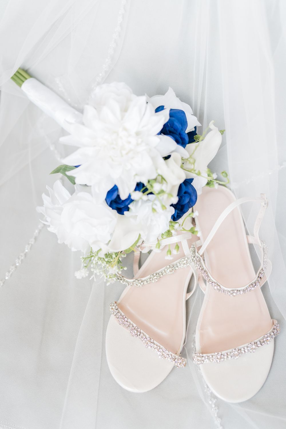 Wedding bouquet with white and blue flowers next to sparkly bridal sandals.