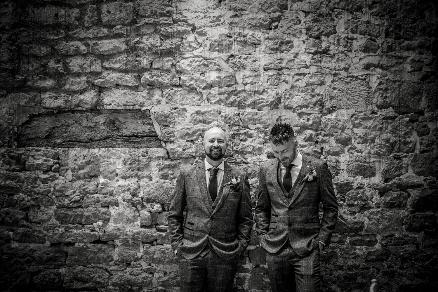 Wedding party gathered against a rustic stone wall in black and white photography.