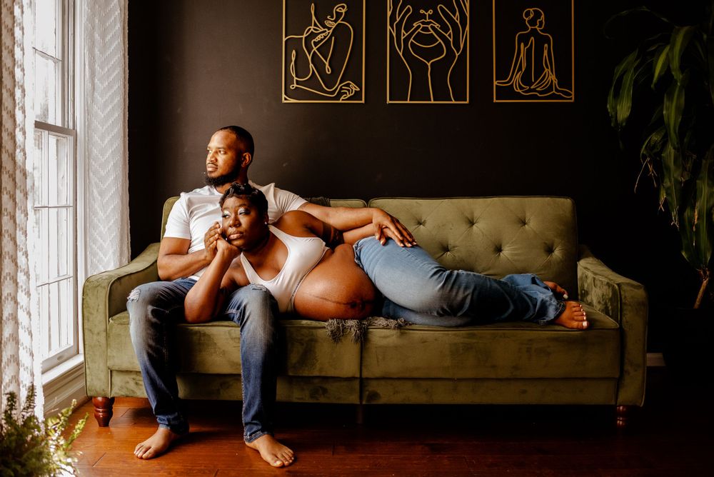 Black couple maternity session on green couch in natural light studio