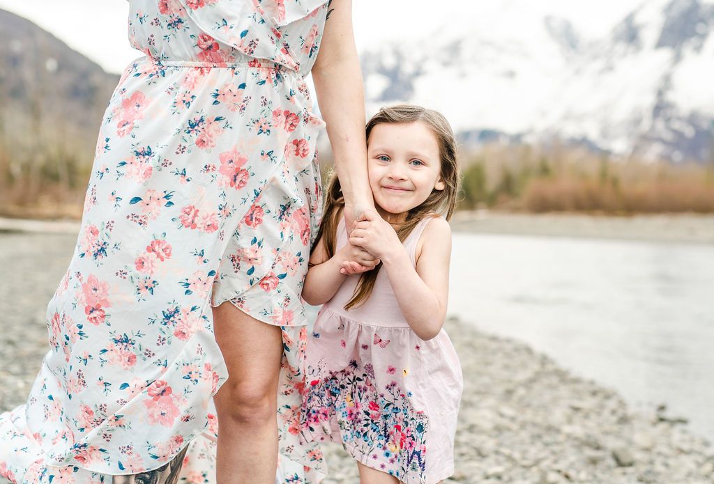 Mother and daughter in matching floral dresses standing by mountain lake.