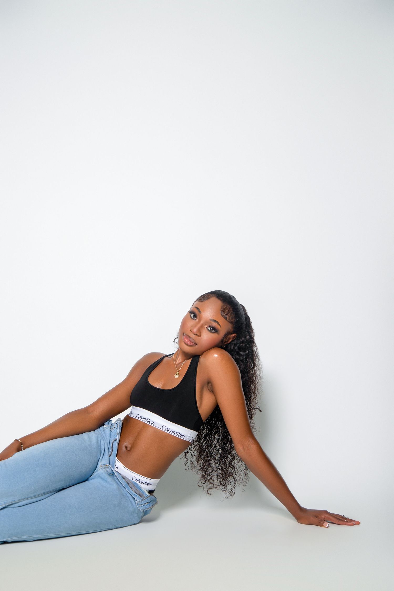 Fashionable model in black crop top and jeans poses casually against white background.
