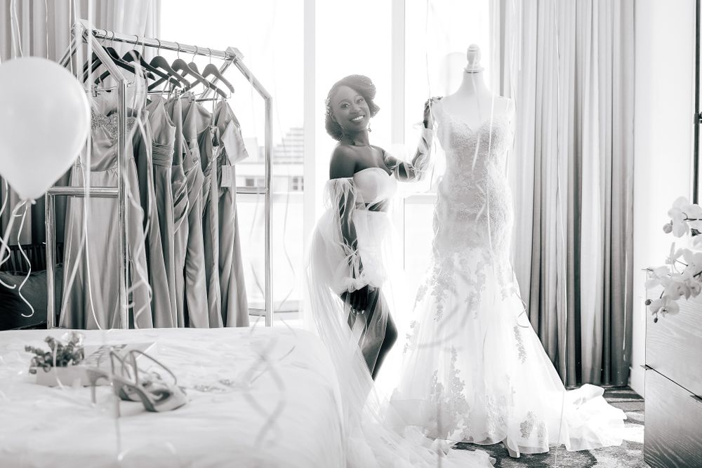 Black and white photo of bride admiring wedding gown on mannequin in bright bridal suite.