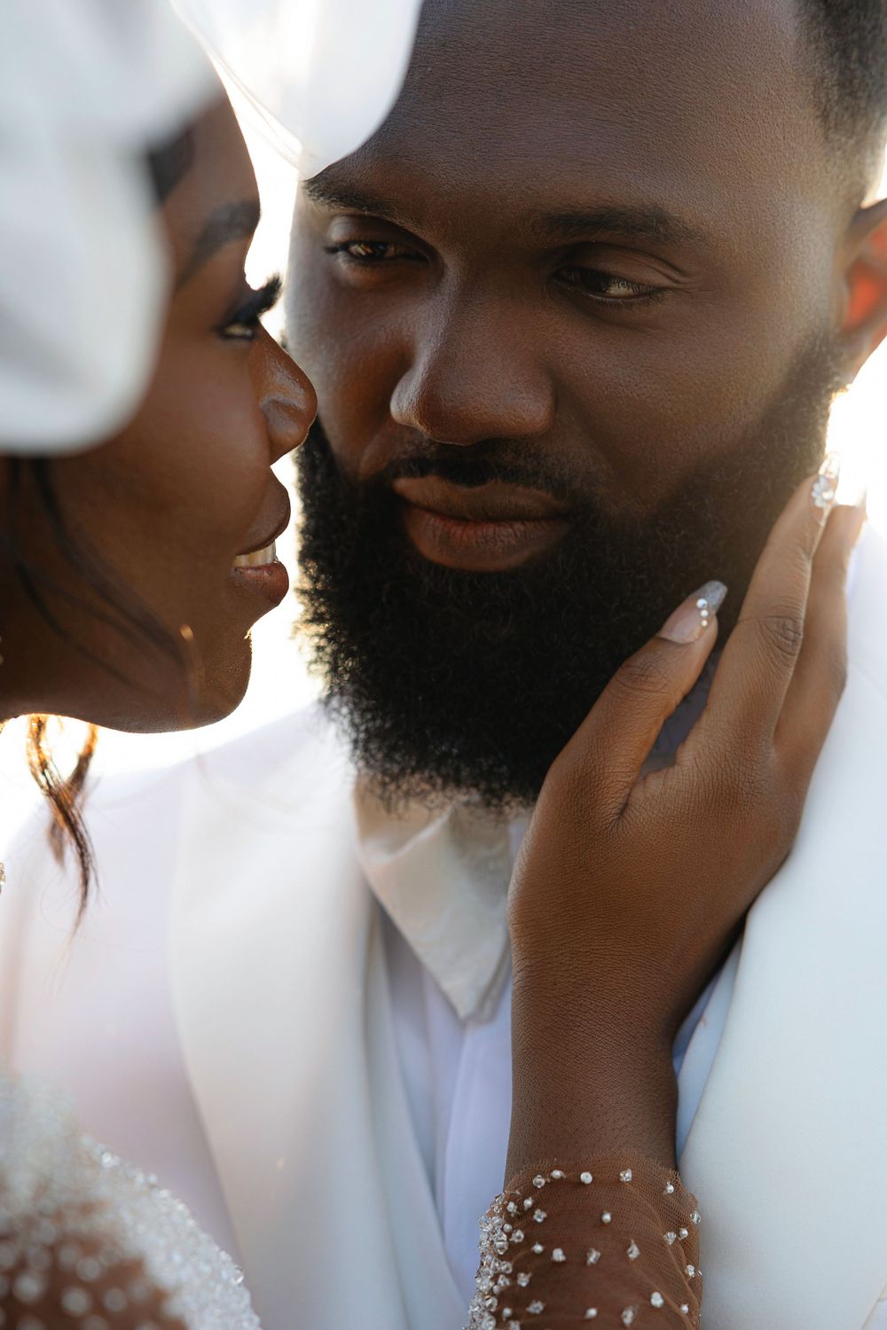 Intimate close-up portrait of a Black bride and bearded groom in white wedding attire.