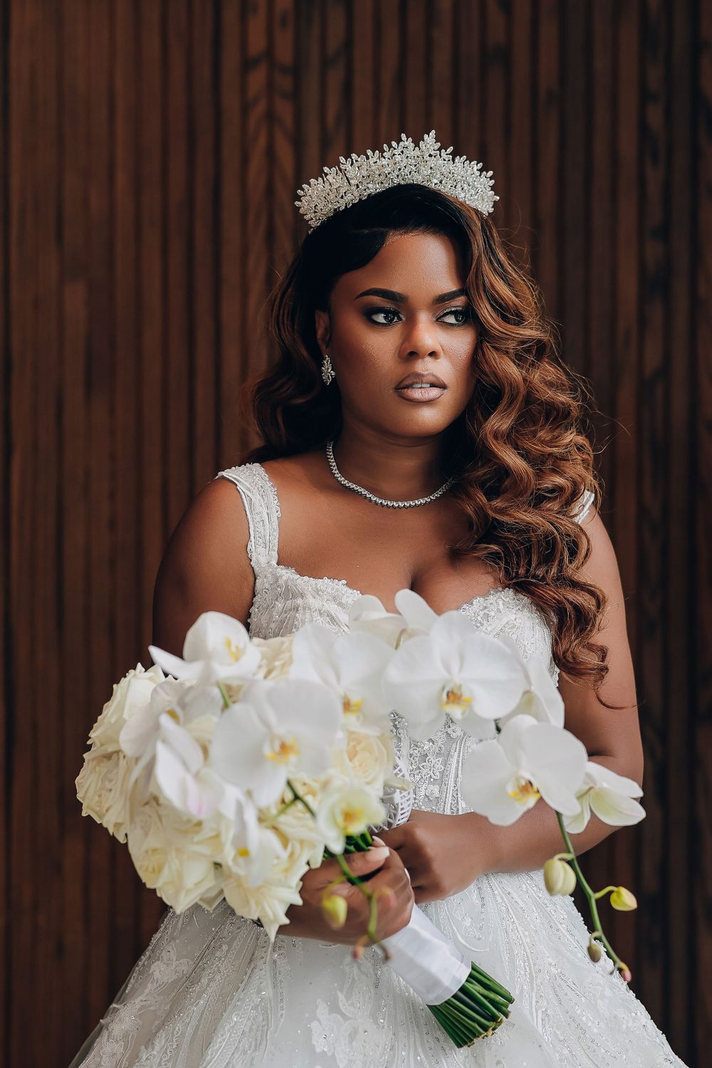 Stunning Black bride in a beaded white gown and crown holding a white orchid bouquet.
