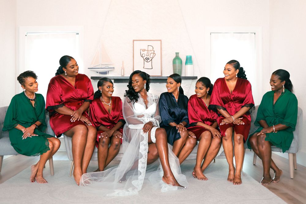 Bride surrounded by bridesmaids in red and green robes sharing joyful moments before wedding ceremony.