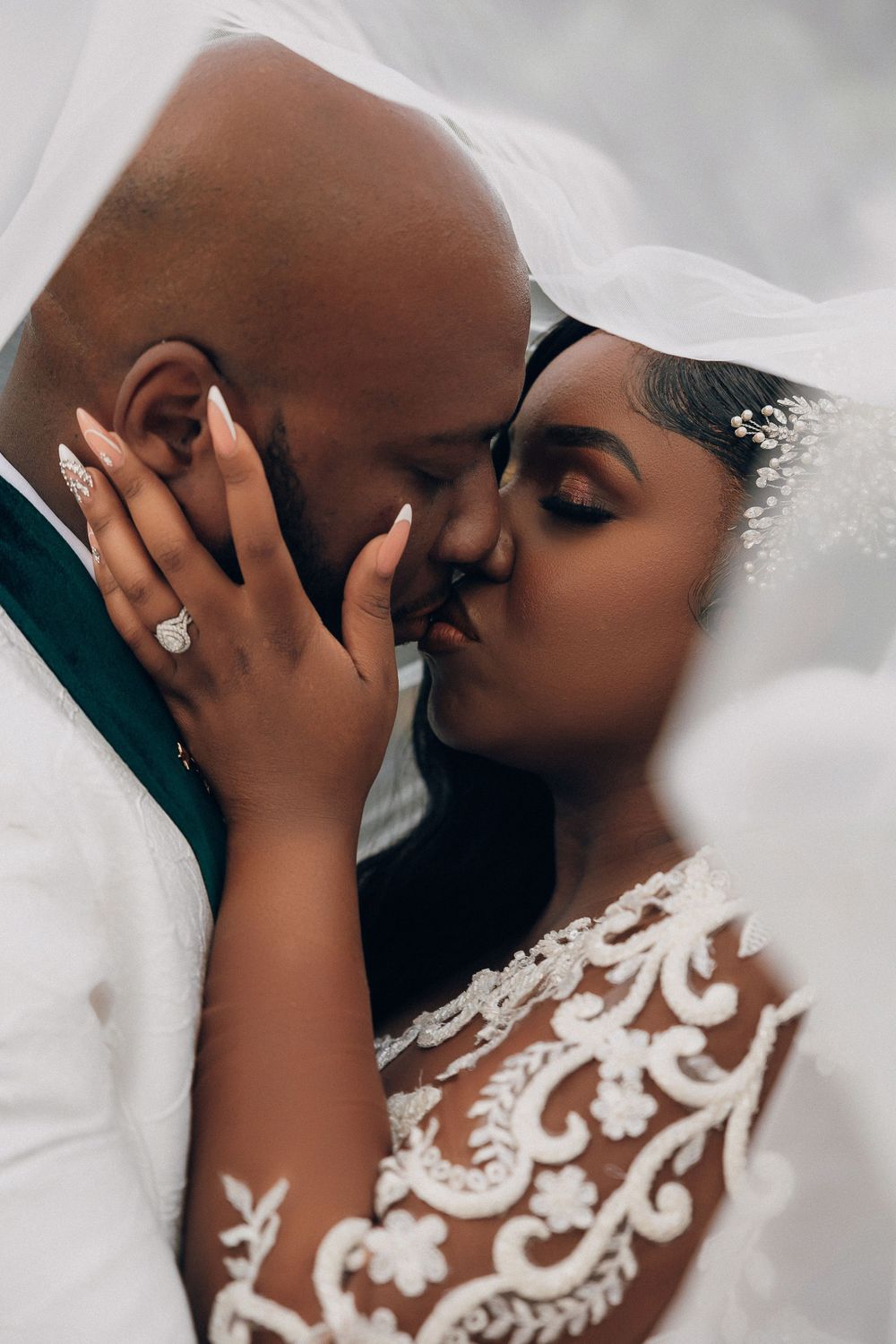 Romantic close-up of a Black bride and groom sharing a kiss beneath a flowing white veil.