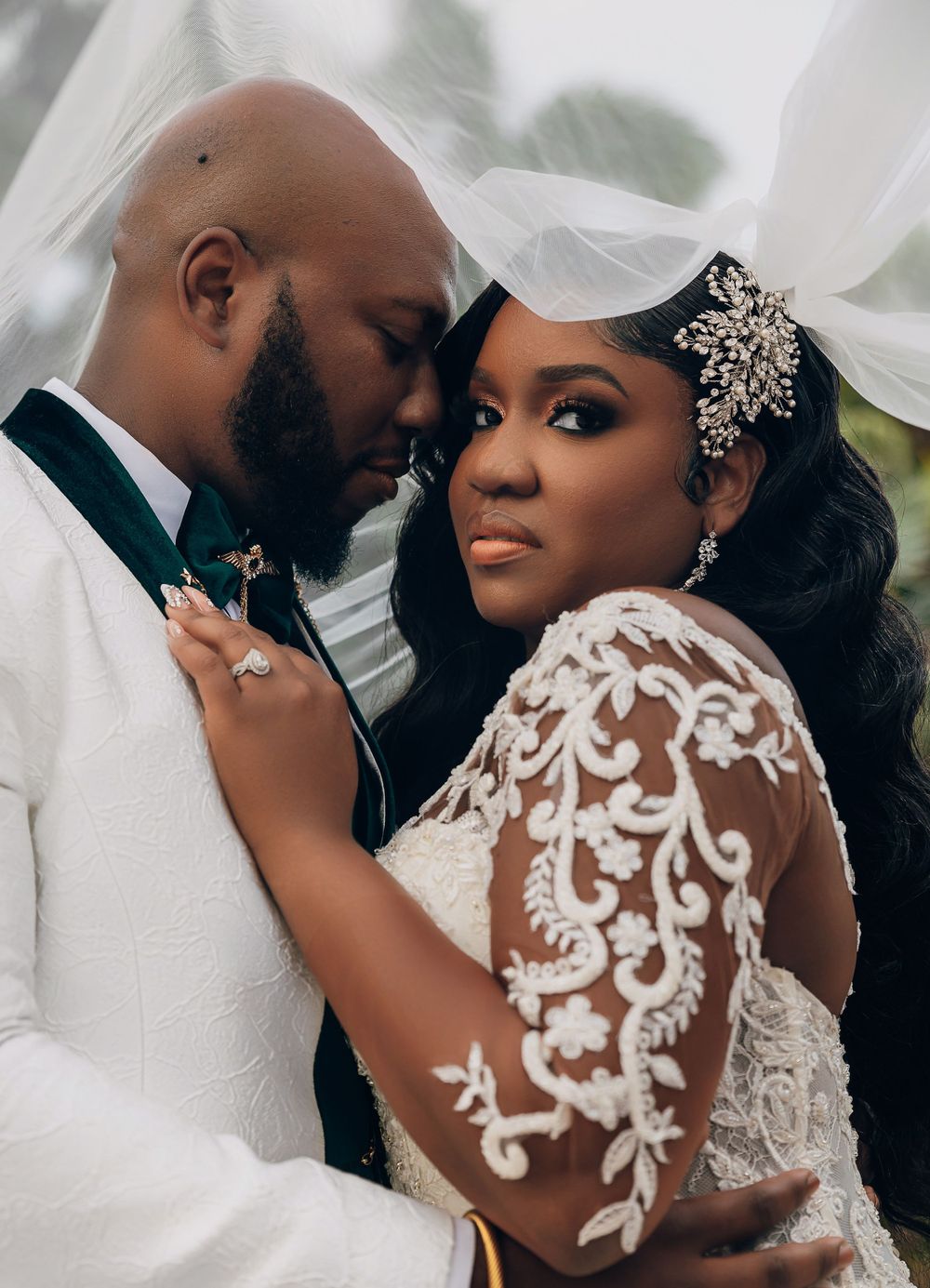 Romantic Black bride and groom embracing under a veil, bride in lace gown with jeweled headpiece.