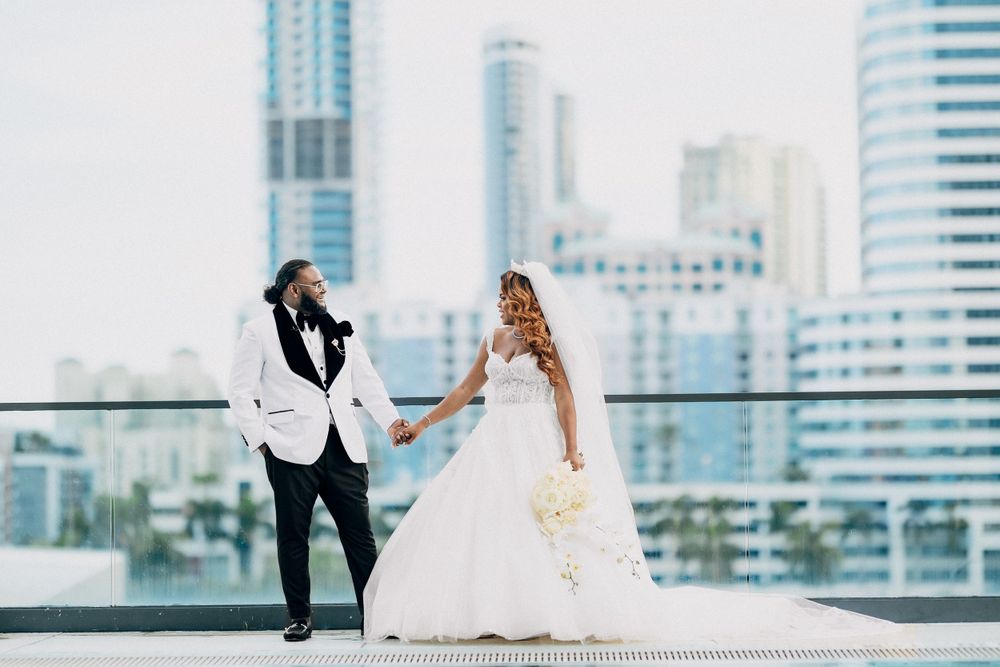 Bride and groom hold hands on rooftop with stunning city skyline backdrop on wedding day.