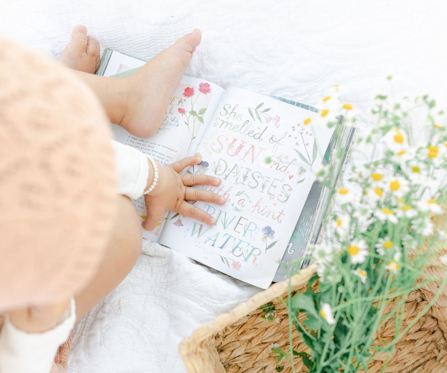 Baby's hands touching a book with flowers in soft natural lighting.Captured by Chelsee Rawe Photography