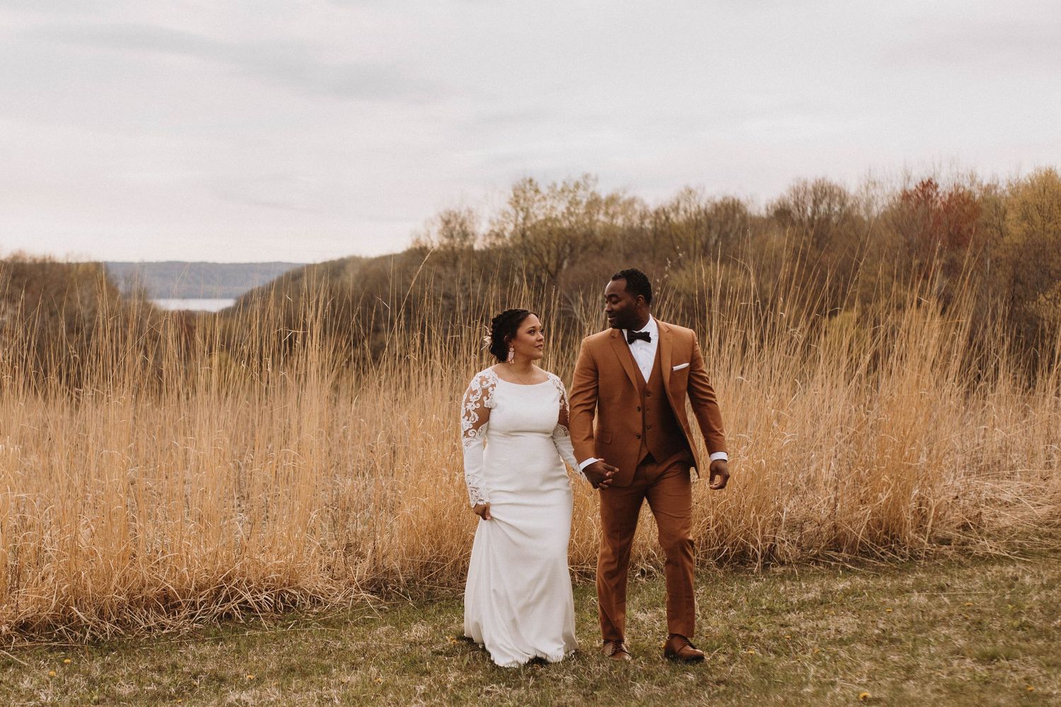 Wedding couple walks by a prairie overlooking the bluffs of the Mississippi River at Maidenwood Wedding and Events