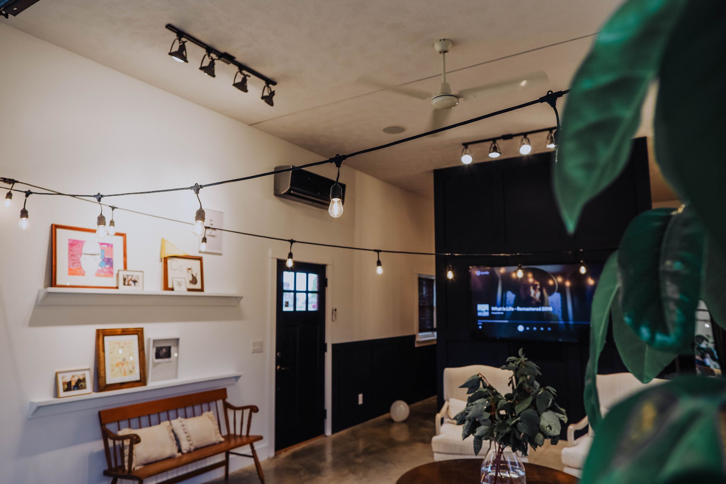 Interior of a stylish room with track lighting, wooden benches, and framed artwork on white walls.