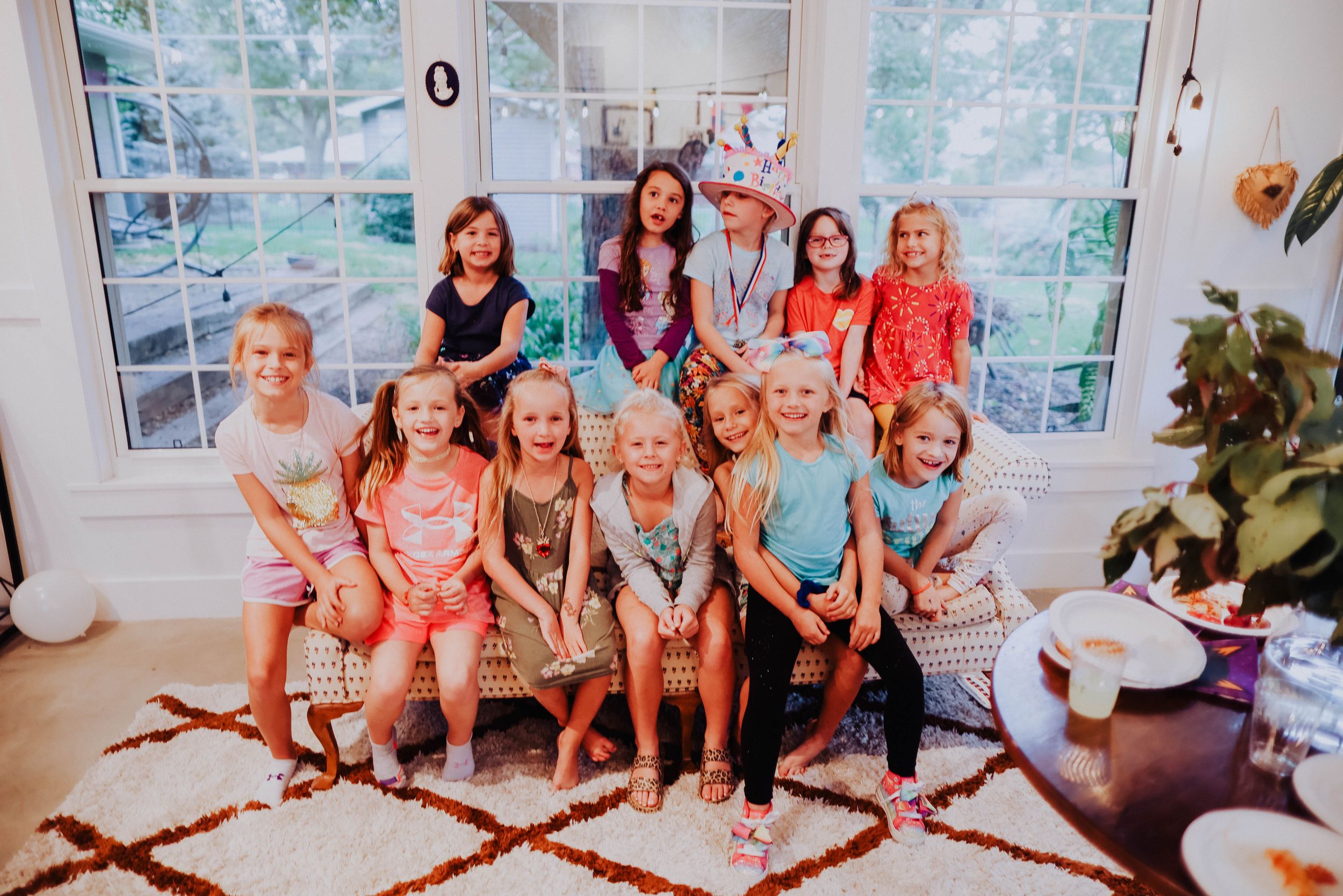 A group gathered on a patterned rug in front of large windows during a celebration.
