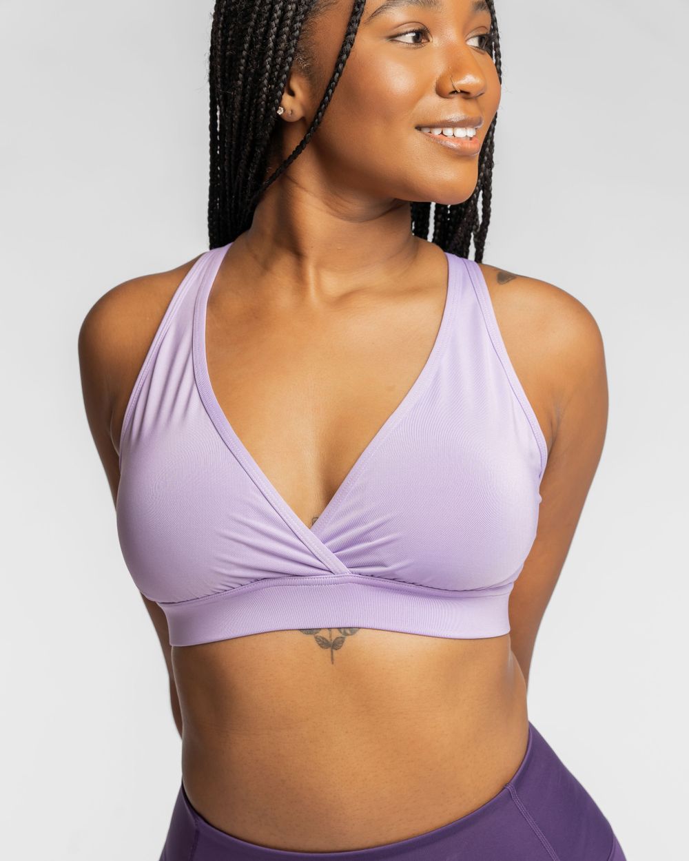 Athletic sports bra in soft lilac color with crossover v-neck design and comfortable racerback straps against light background. Brand photo.