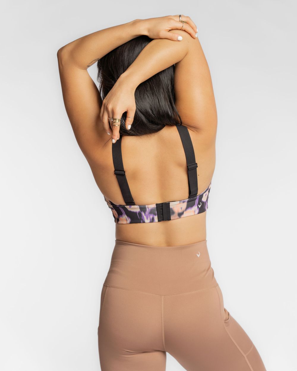 Back view of athletic woman in nude high-waisted leggings and patterned sports bra with adjustable straps. Handful activewear brand photo.