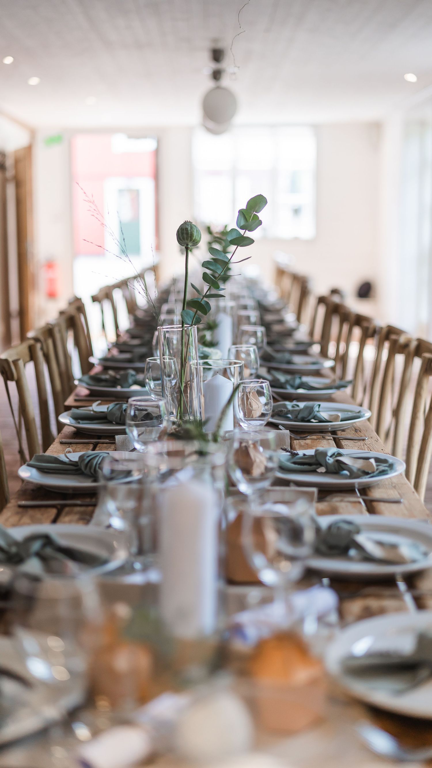 Long rustic wooden banquet table set with sage green napkins and eucalyptus centerpieces for a wedding.