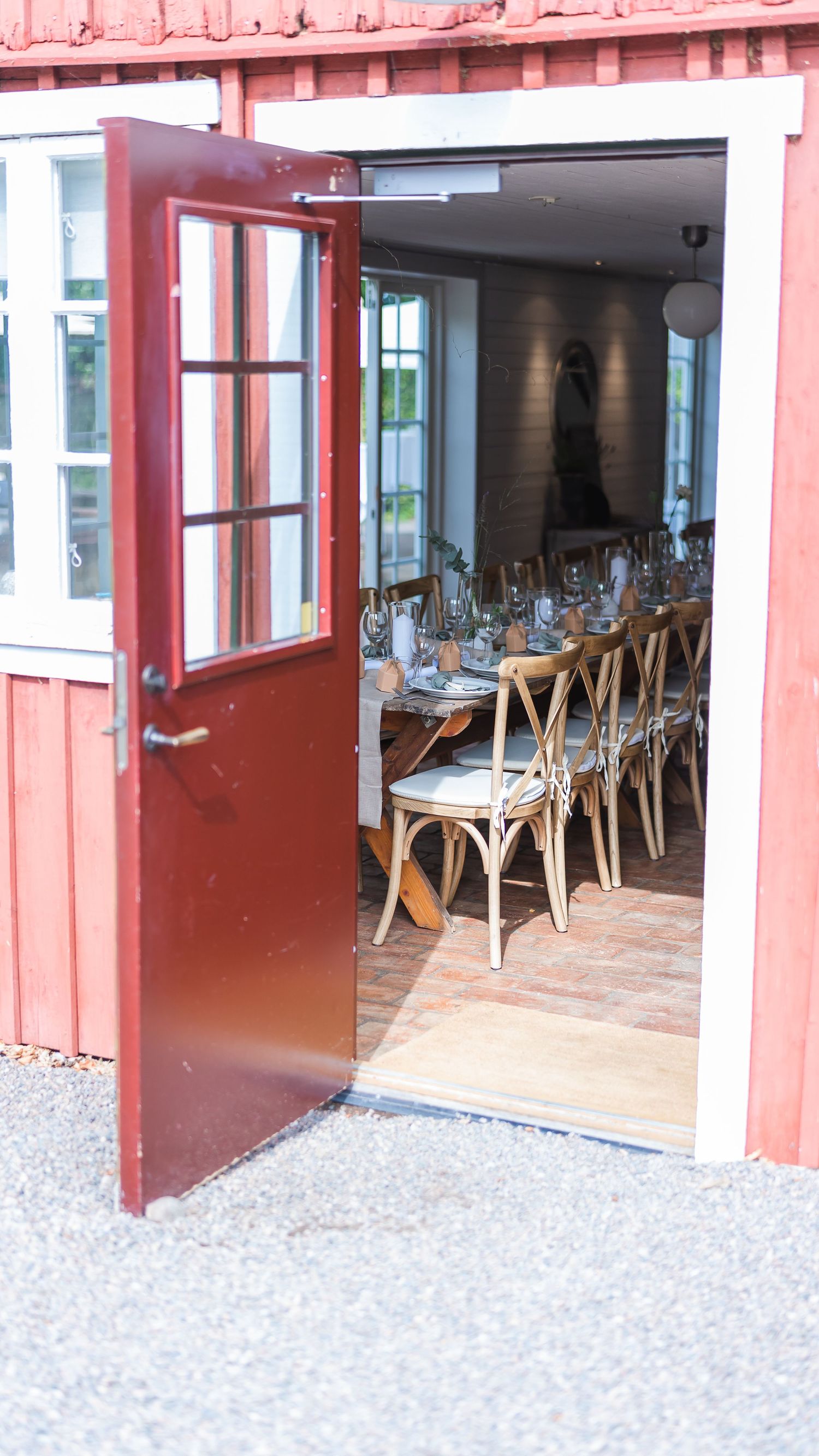 Open red barn door revealing a long elegantly set wedding reception table inside a rustic venue.