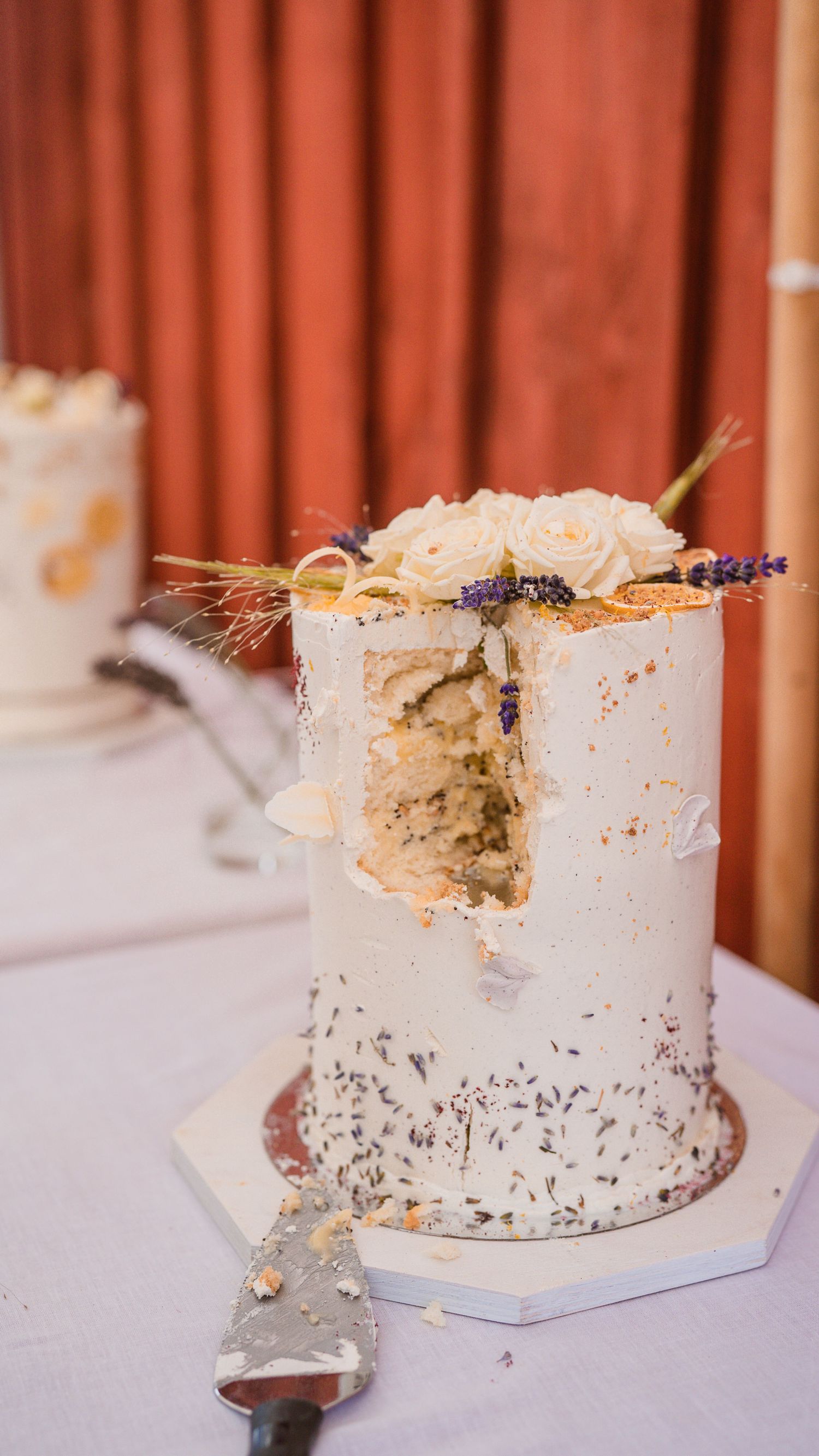Elegant white wedding cake decorated with roses and lavender, with a slice removed revealing layered interior.