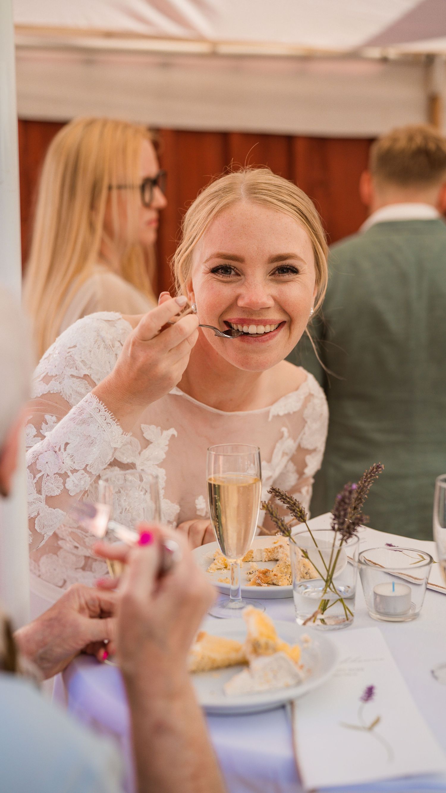 Smiling blonde bride enjoying wedding cake with champagne at the reception dinner table.
