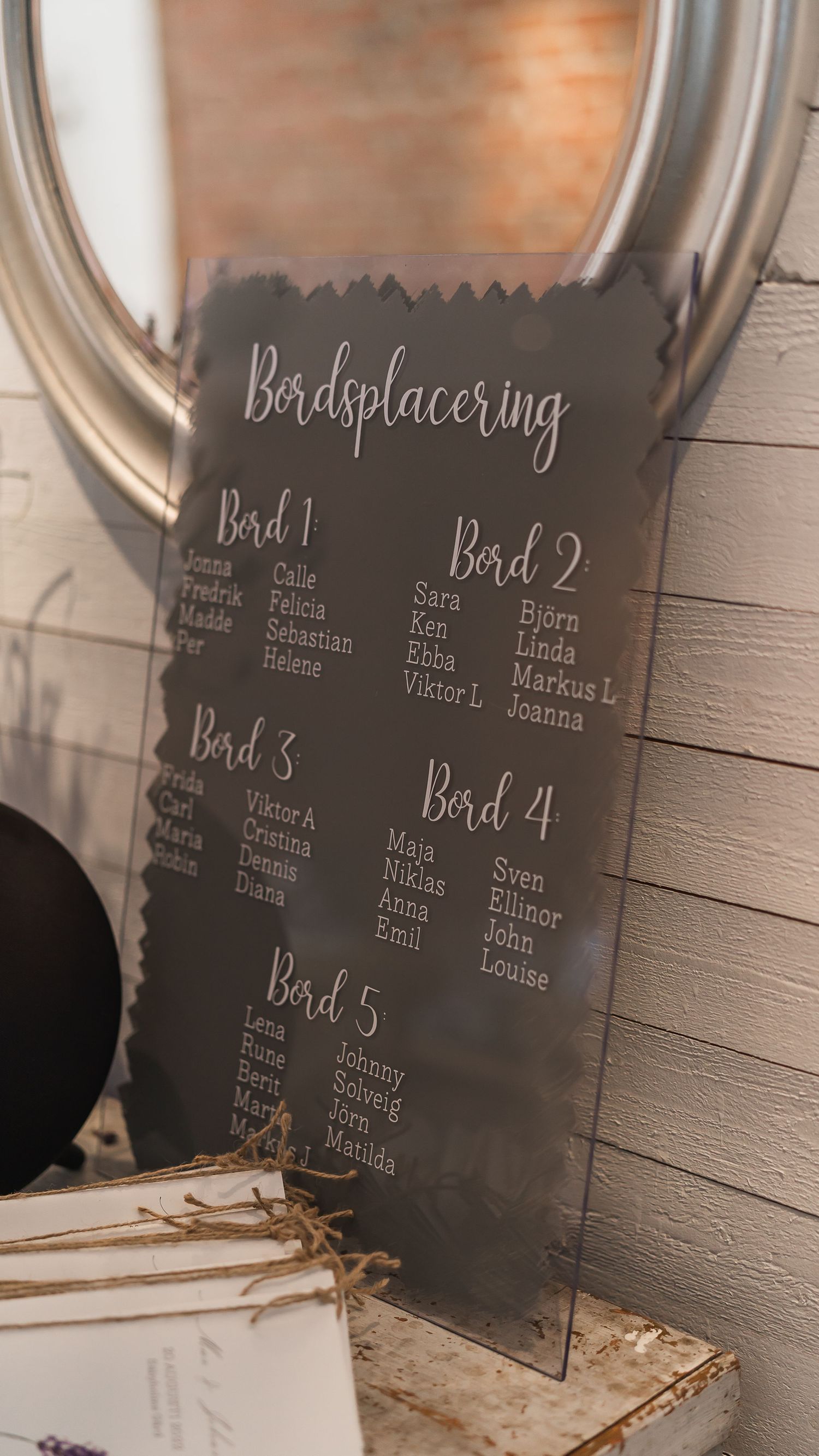 Elegant acrylic wedding seating chart sign reading Bordsplacering displayed on a decorative stand.