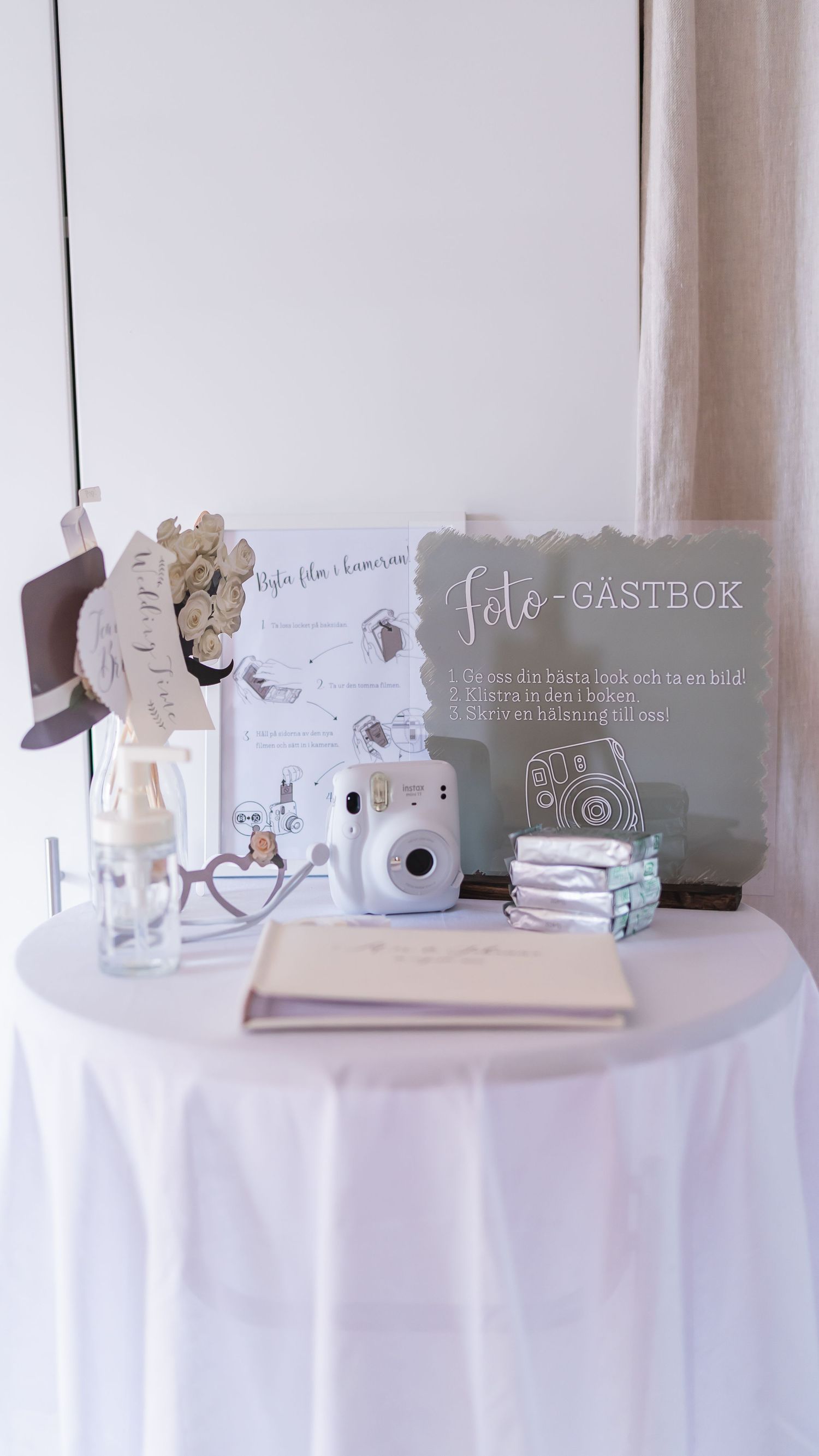 Wedding photo guestbook table with Instax camera, sign, props, and guest book on a white draped table.