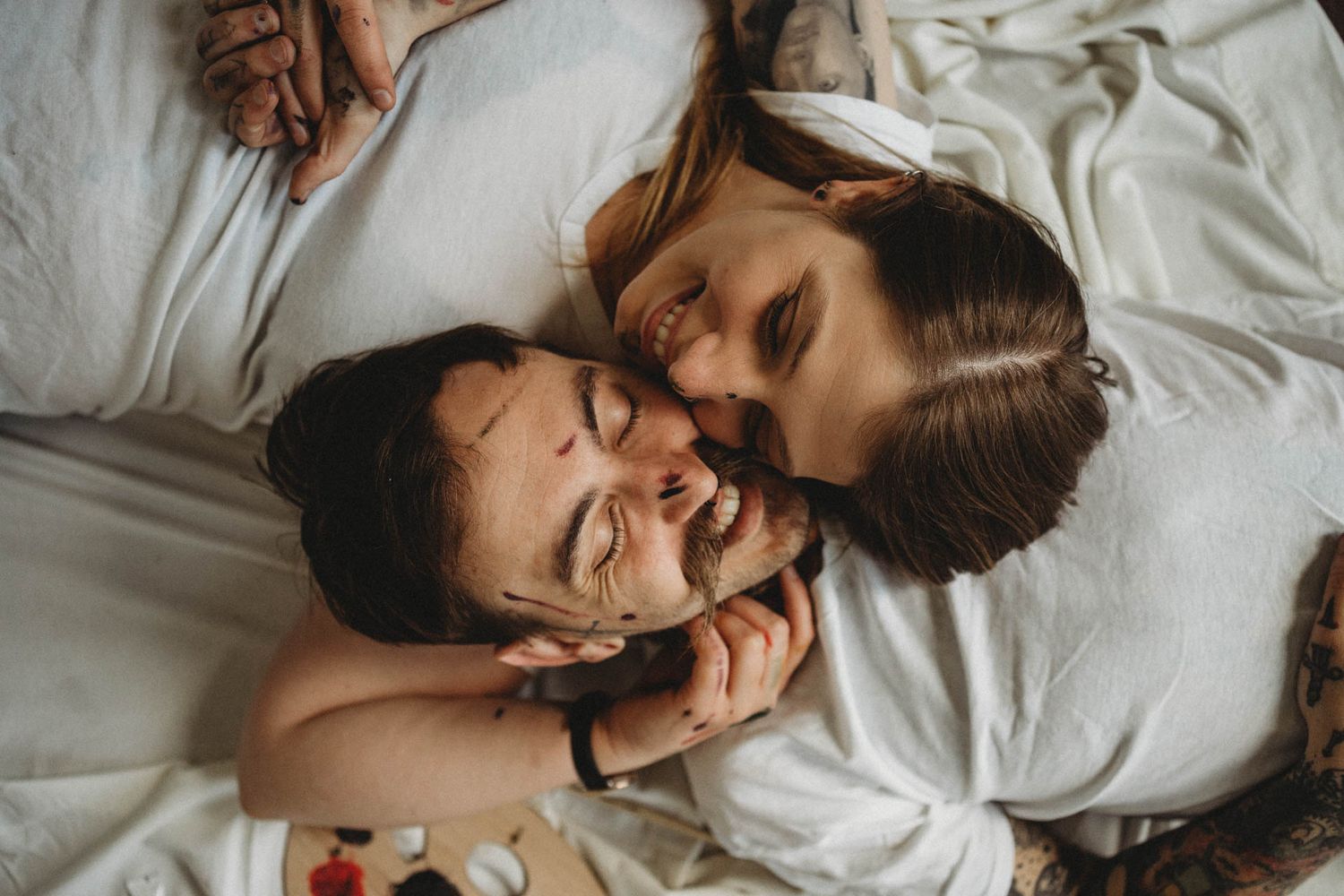 Intimate moment of laughter and joy shared while laying on white bedding.