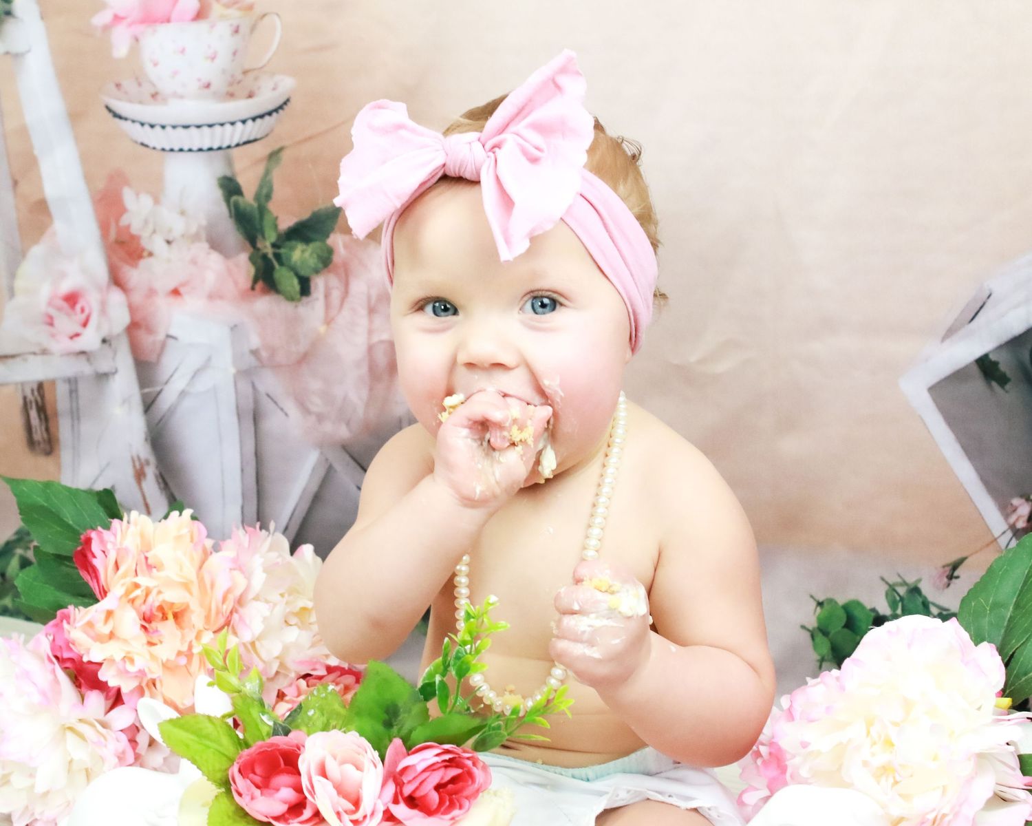 Baby in pink bow smashing pink and white cake during first birthday cake smash photo session.