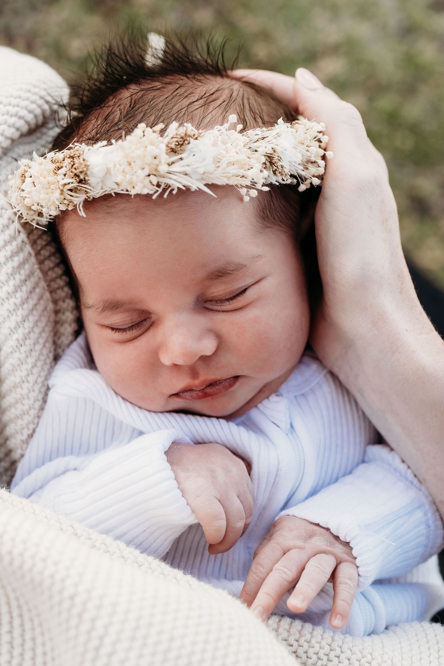 Close-up view of a sleeping newborn baby wearing white and wrapped in soft textiles with delicate lace details.