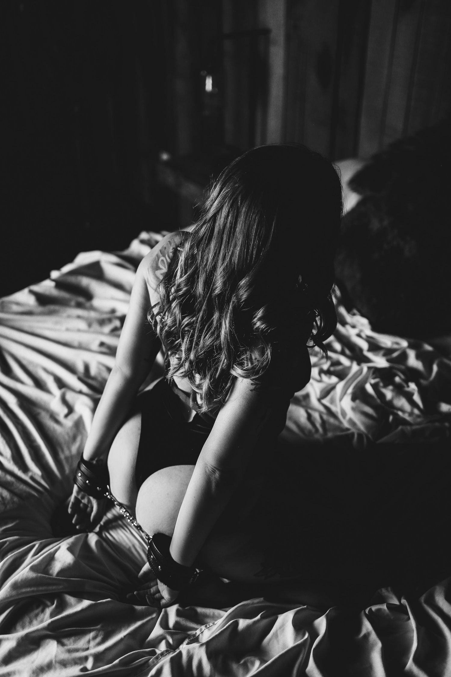 Intimate black and white boudoir photo with soft lighting on rumpled bedsheets.