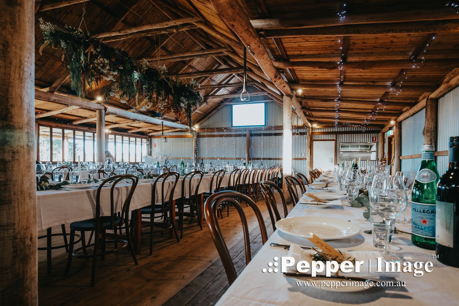 Elegant rustic barn wedding reception with long tables, bentwood chairs, greenery garlands, and soft ambient lighting.