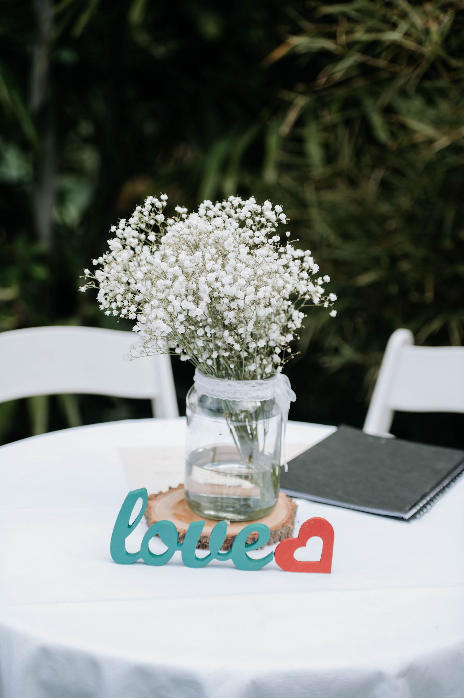 Baby's breath flower arrangement in mason jar with colorful love sign on white table.