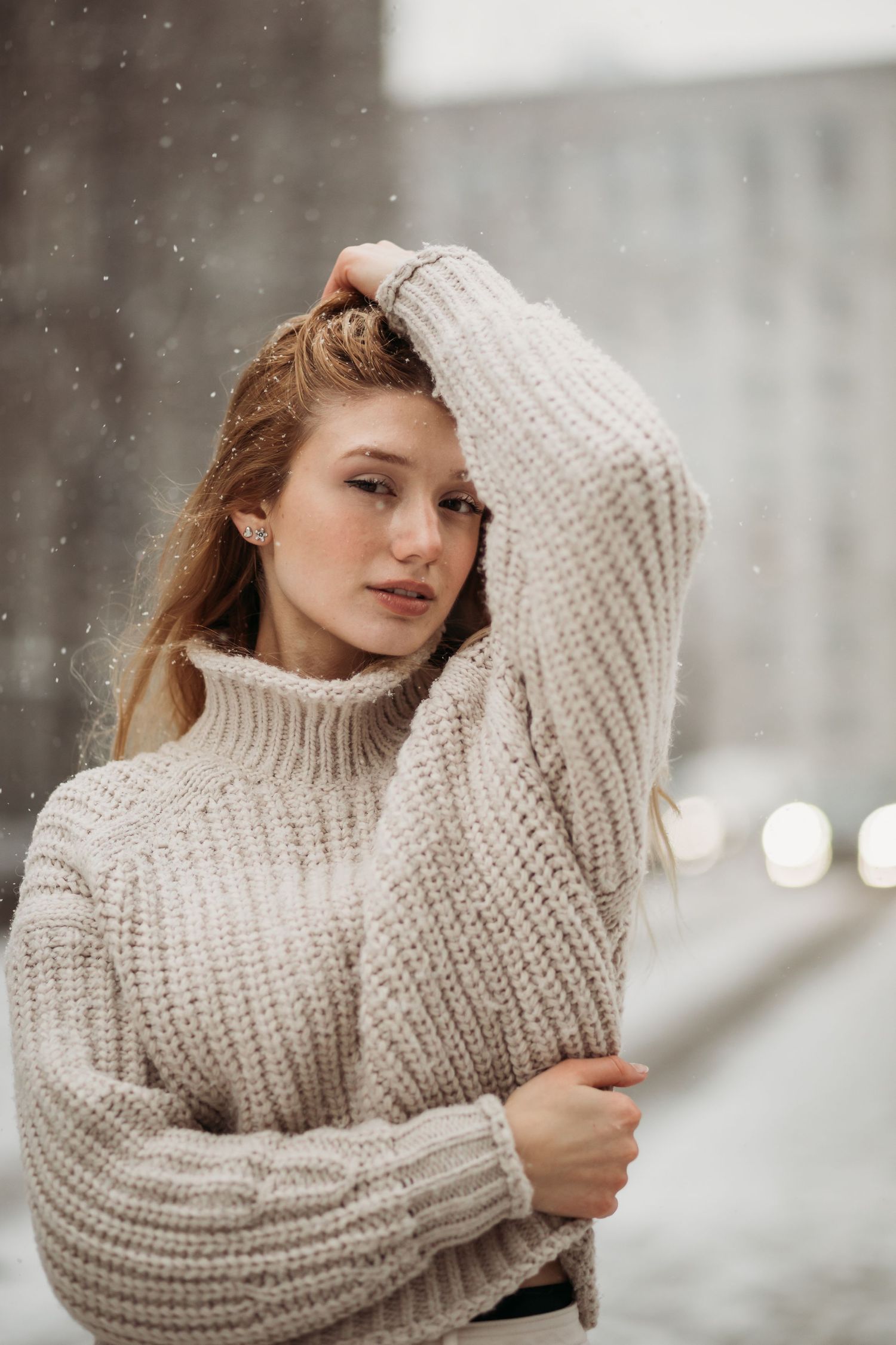 Atmospheric winter portrait with person in chunky knit sweater against urban backdrop.