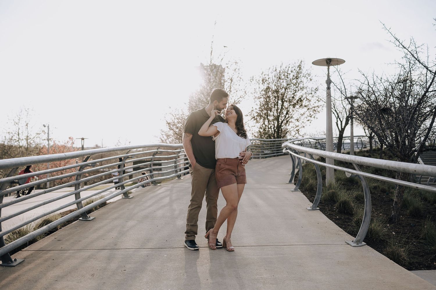 A couple embraces on a modern walkway with railing during a casual photoshoot.