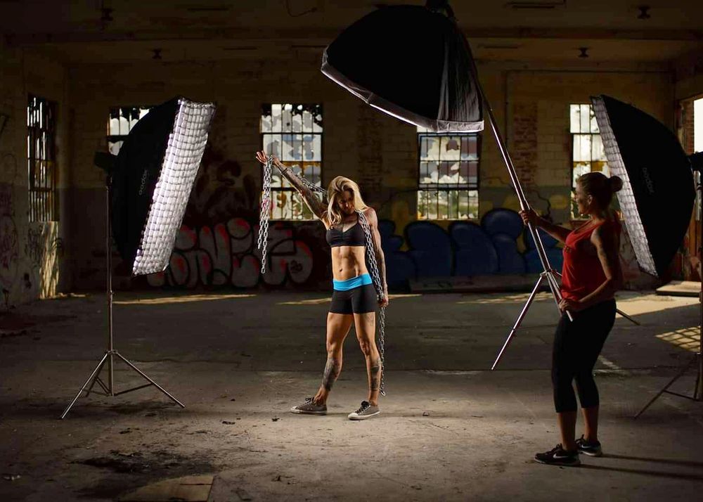 Fashion photoshoot in abandoned warehouse with lighting equipment and model posing.